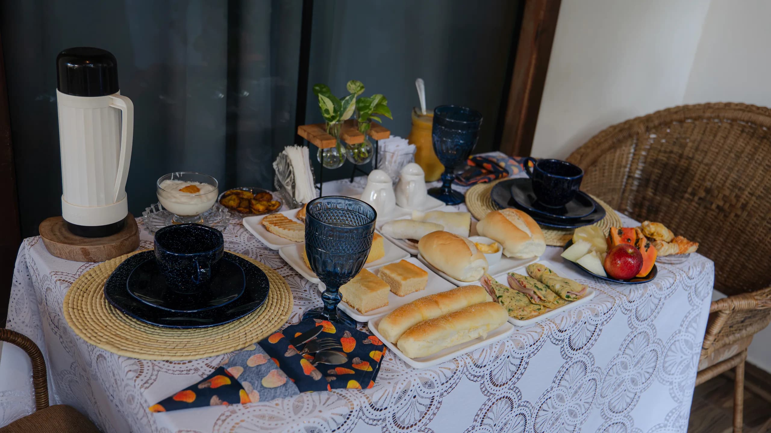 Mesa de café da manhã com louça azul, pães, frutas e suco natural