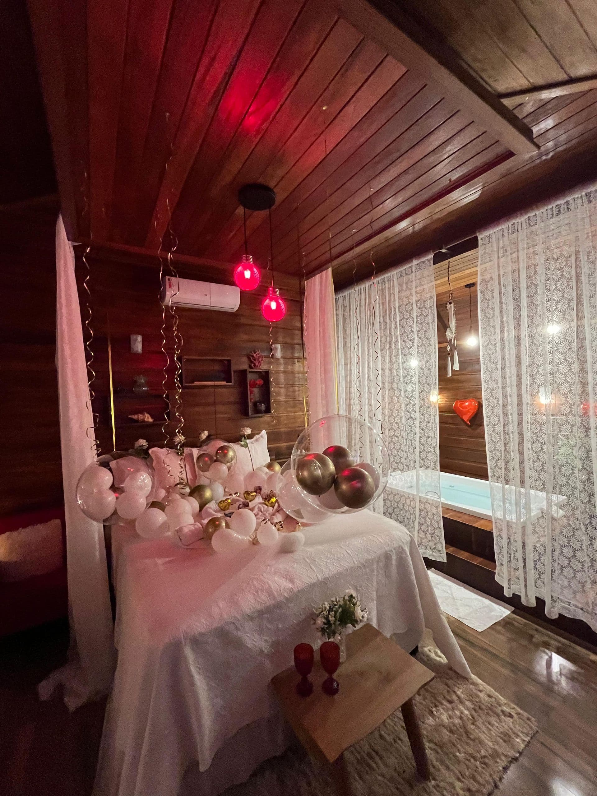 Banheira de hidromassagem do Chalé Master, vista através de cortinas de renda com iluminação em tom vermelho