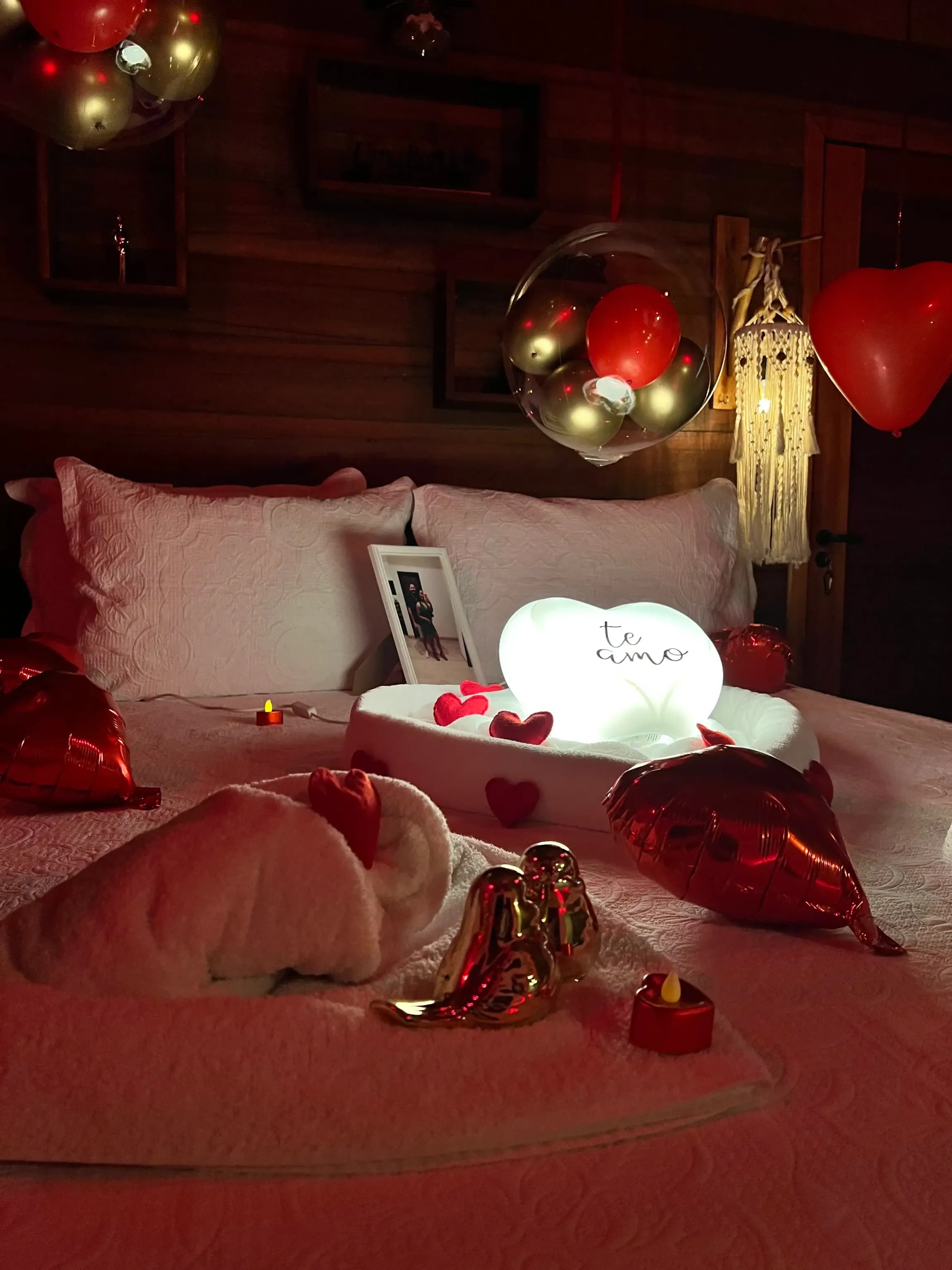 Cama decorada para noite romântica com balões, velas e luz suave