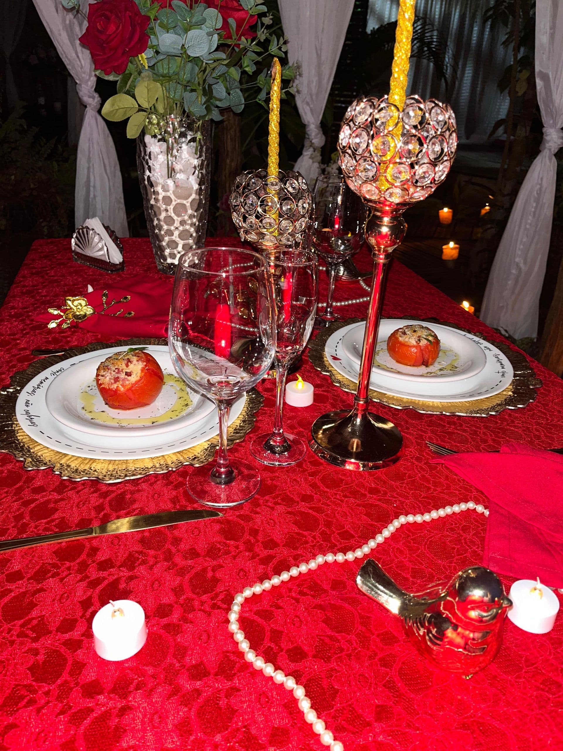 Mesa romântica posta com toalha vermelha, taças de cristal e prato principal decorado