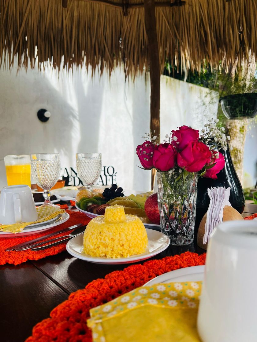 Mesa de café da manhã com cuscuz, frutas, suco e rosas sob cobertura de palha