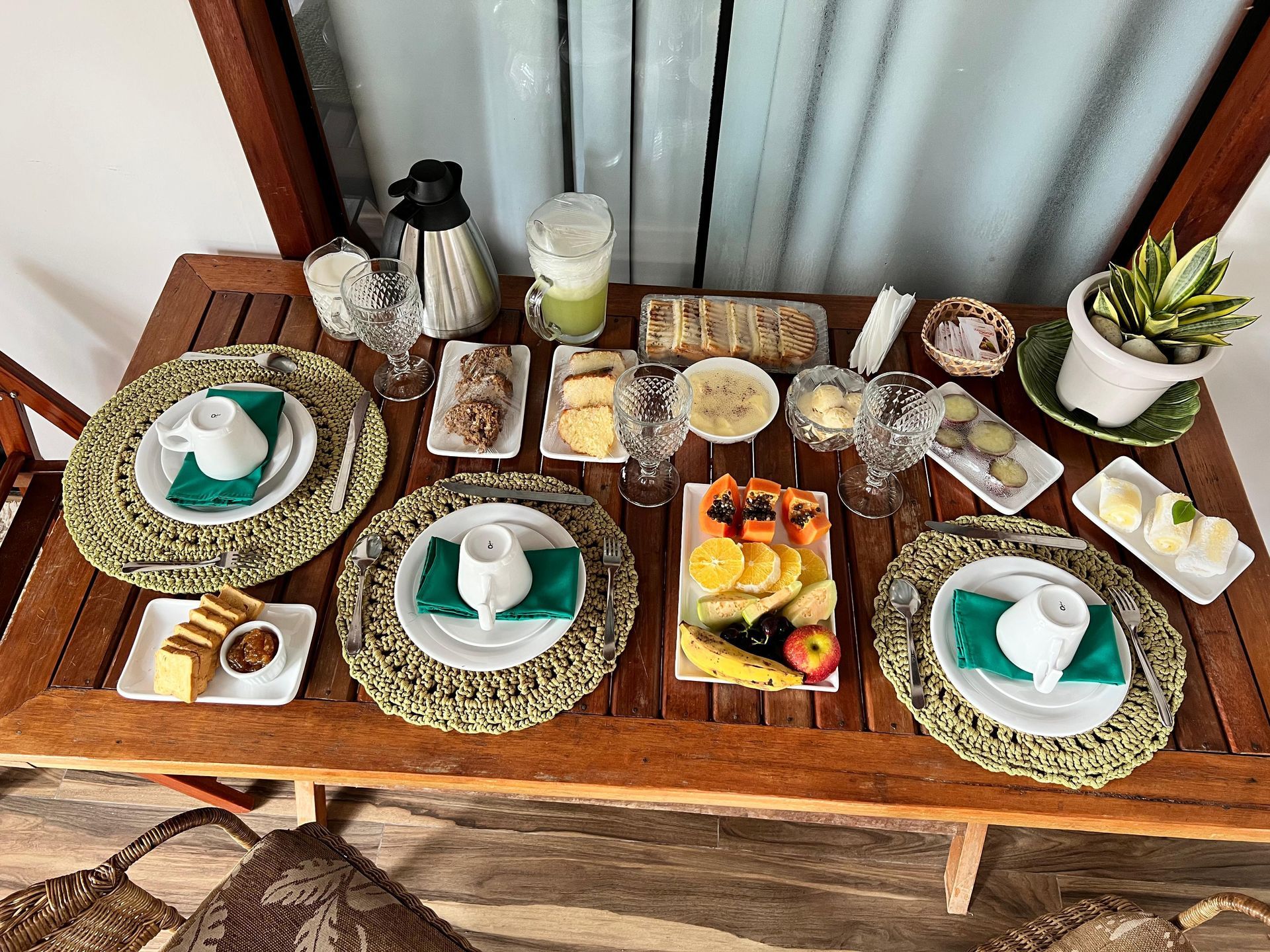 Mesa de café da manhã vista de cima, com bolos, frutas e sucos servidos em jogo americano verde